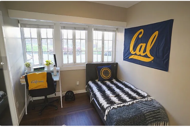 Cozy bedroom with a study nook, featuring a single bed, vibrant decor, and ample natural light through large windows. - La Loma Co-Living Community Apartments
