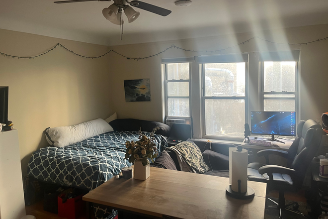 Bedroom/Sitting area with ceiling fan and window A/C unit. - Summer Sublet: Studio Apartment, Downtown Evanston, Start Date Negotiable