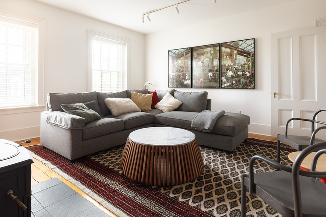 Living room —Hand‑knotted Bokhara wool rug, Pottery Barn sectional sofa, marble-top drum coffee table, and large south-facing windows. - 61 OTIS — Furnished Historic Residence, East Cambridge near Kendall Square Townhome