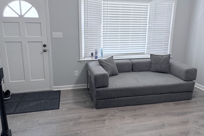 Living room sitting area featuring a large bay window for natural light and a comfortable sofa provided for shared use. - Private BR/Bath for Rent in 2BR Condo - All-Inclusive & Direct Bus to UNC