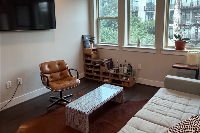 Bright living room with wall-mounted smart-TV and large windows with privacy blinds. - Quiet 1BR near campus. Modern & spacious, near METRORail. Unfurnished ($1,850) or furnished ($2,200) Apartments
