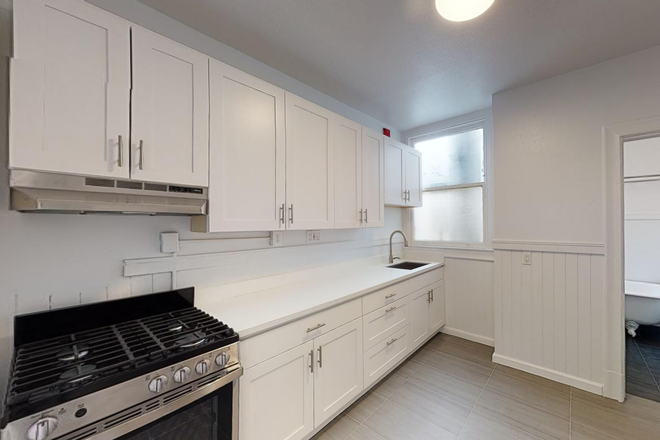 Kitchen with cabinets, stainless steel appliances, and a sink beneath a window, opening to a room with a bathroom - 2510 Bancroft Way Apartments