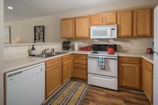 The kitchen has plenty of storage cabinets, a stovetop, oven, microwave, ventilation fan, dishwasher, and fridge. - Mountaineer Village Apartments