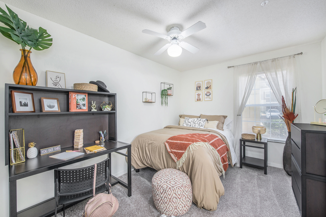 A cozy bedroom with a bed, desk, and soft natural lighting from the window. - 42N Apartments