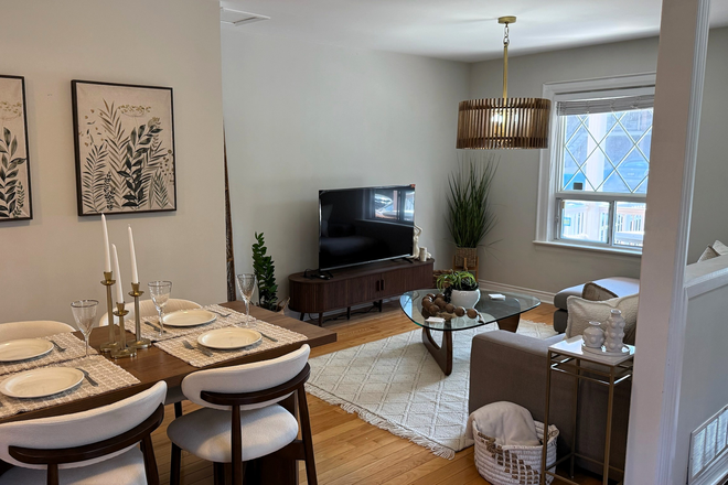 Stylish boho living room featuring elegant gold accents, a dining table that seats 4, and a large flatscreen smart TV. - Furnished 2BR Main-Floor Suite with Laundry & Parking near St. Clair West
