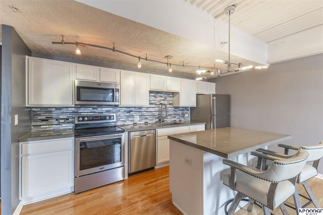 Modern kitchen featuring white cabinetry, stainless steel appliances, tile backsplash, and peninsula seating. - Modern, Move-In Ready Midtown Condo Near Major Campuses & Medical Centers