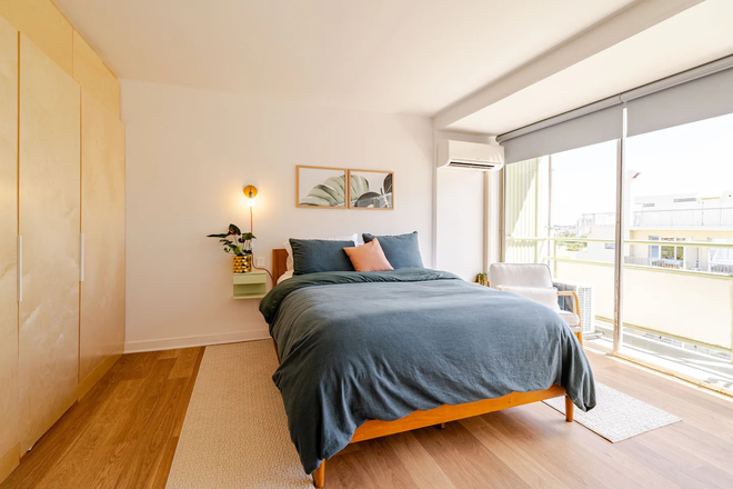 Queen bed with motorized shades, split AC, custom birch wardrobe, and sliding glass door to the lanai. - Renovated Waikiki Studio — Fully Furnished, All Utilities | June 1 Condo