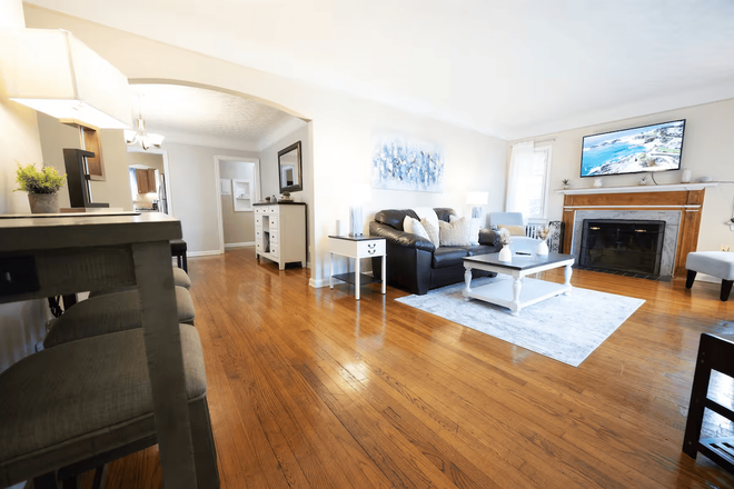 Bright living room with 58” smart TV, comfortable seating, and charging stations throughout. - Cozy Shaker 2BR | 30+ Days | WiFi + Workspace + Garage Apartments