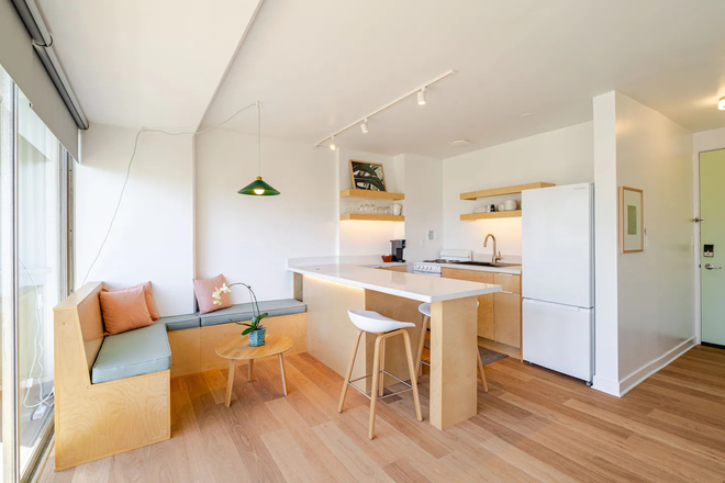 Open-plan living and kitchen with birch finishes, natural light, and lanai access. - Renovated Waikiki Studio — Fully Furnished, All Utilities | June 1 Condo