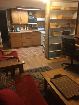 Open living area with sofa, coffee table, shelving, and workspace; kitchen beyond. - Furnished 1BR Garden In-Law – Quiet – Near UC Berkeley – Ideal for Grad/Scholar