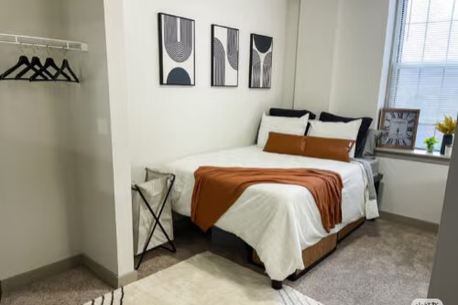 The bedroom is fully furnished with a bed, desk, and storage space. It has large windows for natural light, soft carpeting, and a simple, mo - The academy on Chalers