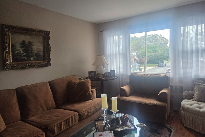 Living room will be transformed into a bedroom upon renting. Brown chair is among furnishings. - Furnished Room for Rent