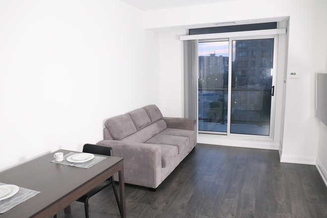 Spacious living room with sofa and television next to sliding balcony door. - 1 Bedroom Apartment Fully Furnished Turnkey UofT UTSC OCMT
