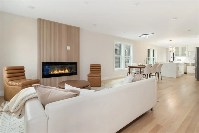 Bright, open-concept living space featuring a modern fireplace and designer lighting. - Steps to Tufts: Sunny 4-Bed at 157 Boston Ave