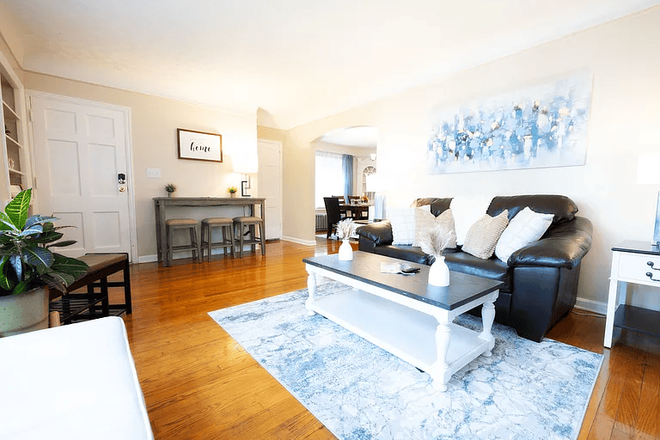 Bright living room with 58” smart TV, comfortable seating, and charging stations throughout for work and downtime. - Cozy Shaker 2BR | 30+ Days | WiFi + Workspace + Garage Apartments