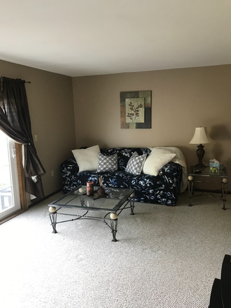 Living room with couch, coffee table, end tables, futon, tv and sliding glass door to patio with furniture and grill. - Heritage Hill Condominium