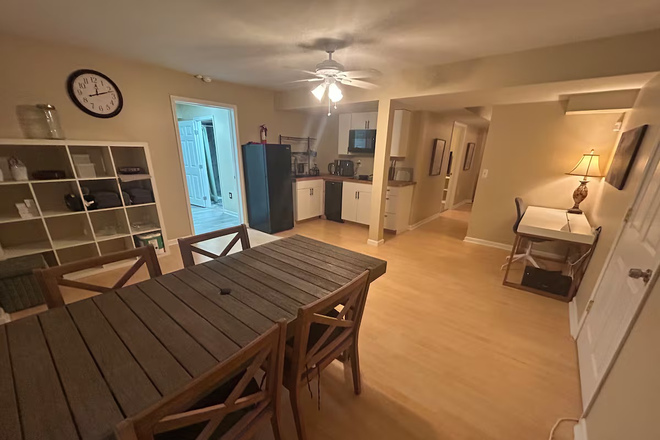 Open-concept dining and living area with warm lighting, views outdoors, seating for six, a working nook, and views into the full kitchen. - Lakefront Furnished Home 3bd/1ba + Hot Tub + Gym + Nature