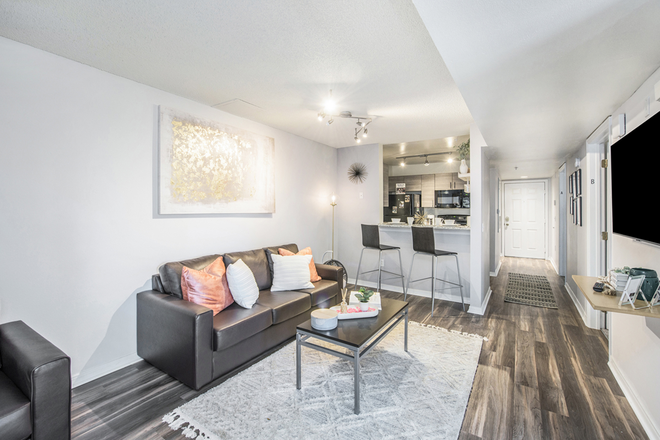 A modern open-concept living room with a sofa, coffee table, and kitchen bar. - 42N Apartments