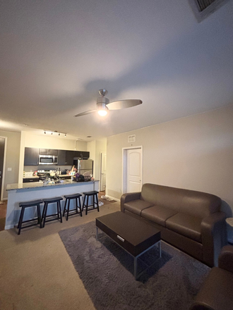 Living room furnished with sofas, kitchen, fridge, stools, and attached balcony - Lark Chapel Hill, Apartment Close to Campus