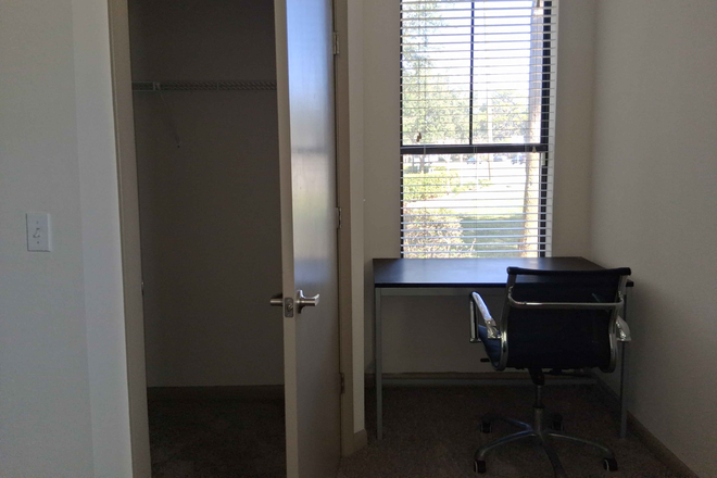 A view of the bedroom's desk, chair, and closet. - The Lark Central Apartment close to campus